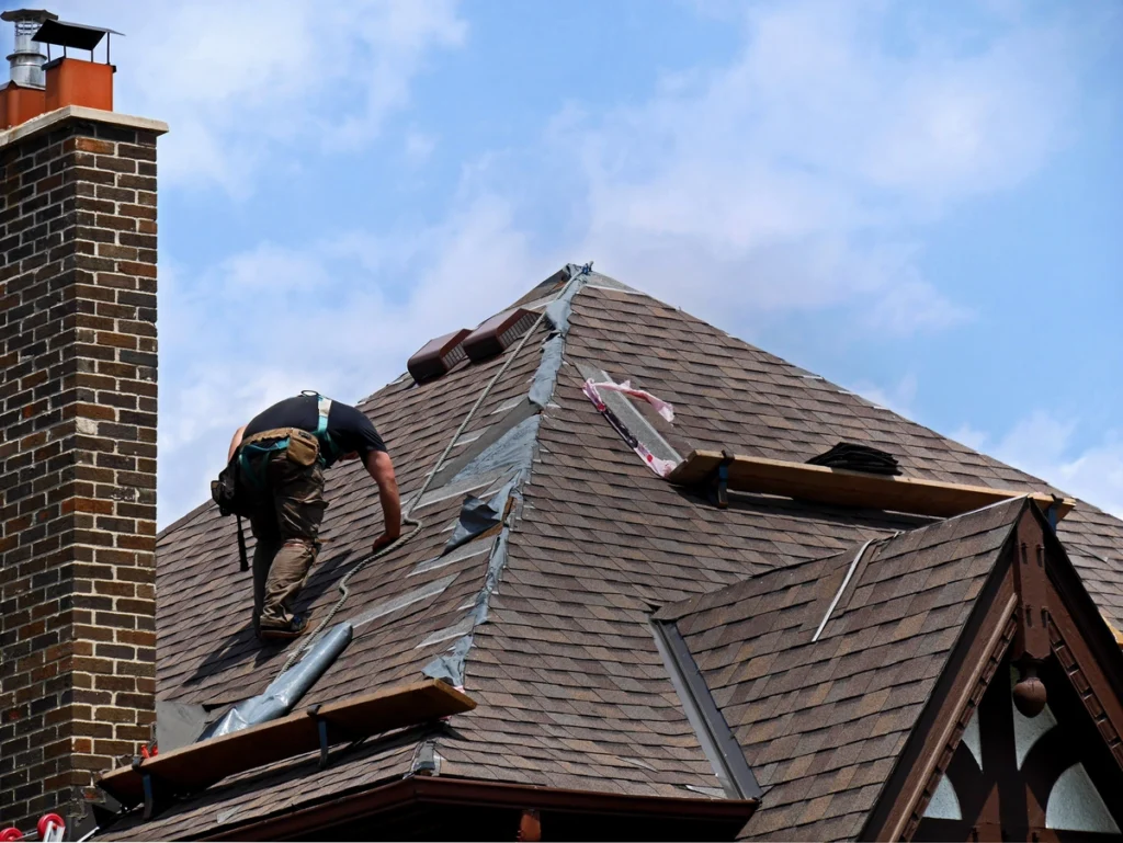 worker repairing the house roof shingles next to chimney